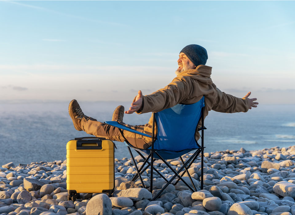 Bearded Man in brown jacket with yellow suitcase relaxing alone and sitting on beach chairs on the seaside at sunrise
