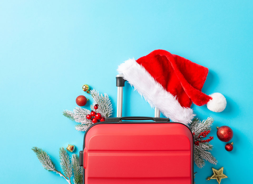 Top view of a red suitcase with santas hat and festive decor on vivid blue backdrop